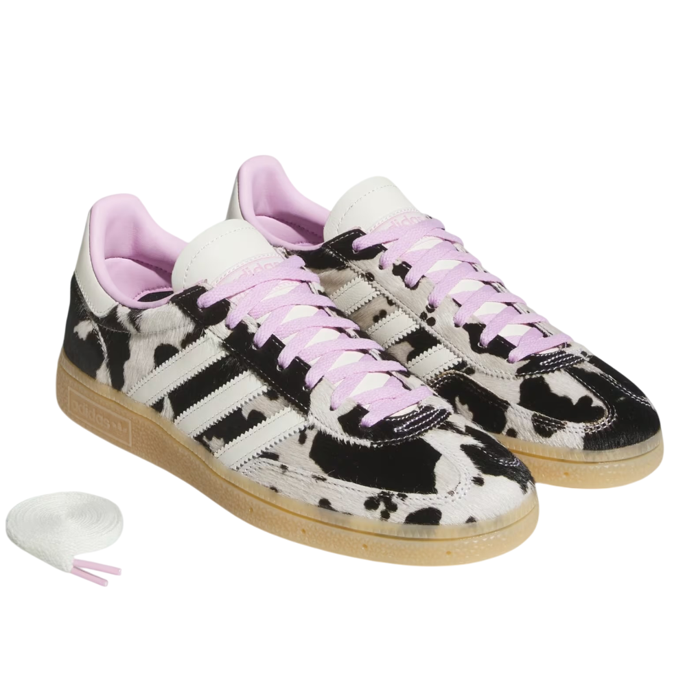Pair of black and white cow print sneakers with pink laces on a white background